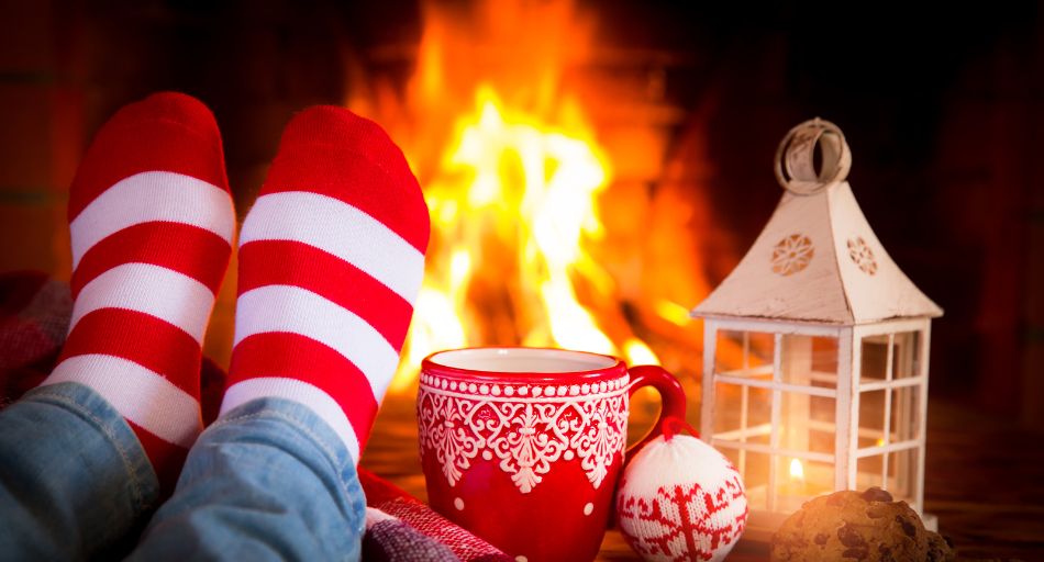 Cozy holiday setting, festive socks, mug and ornament positioned near a roaring fireplace