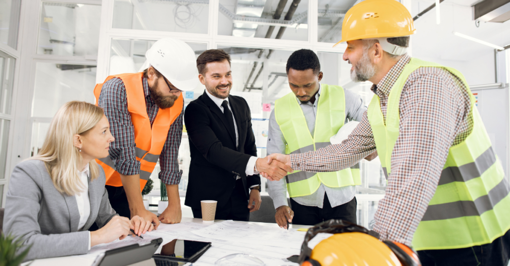 construction professionals in hi vis vests and hard hats at the negotiating table with two businesspeople and shaking hands