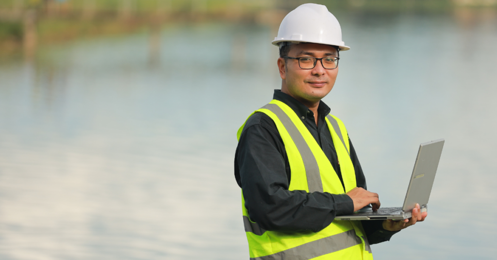 environmental engineer wearing hi vis vest and white hardhat holding laptop at environmental cleanup site